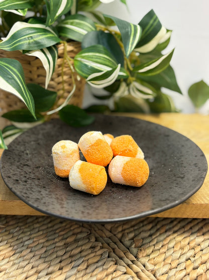 A plate of orange and white mini bath bombs displayed on a wooden surface with a plant in the background.